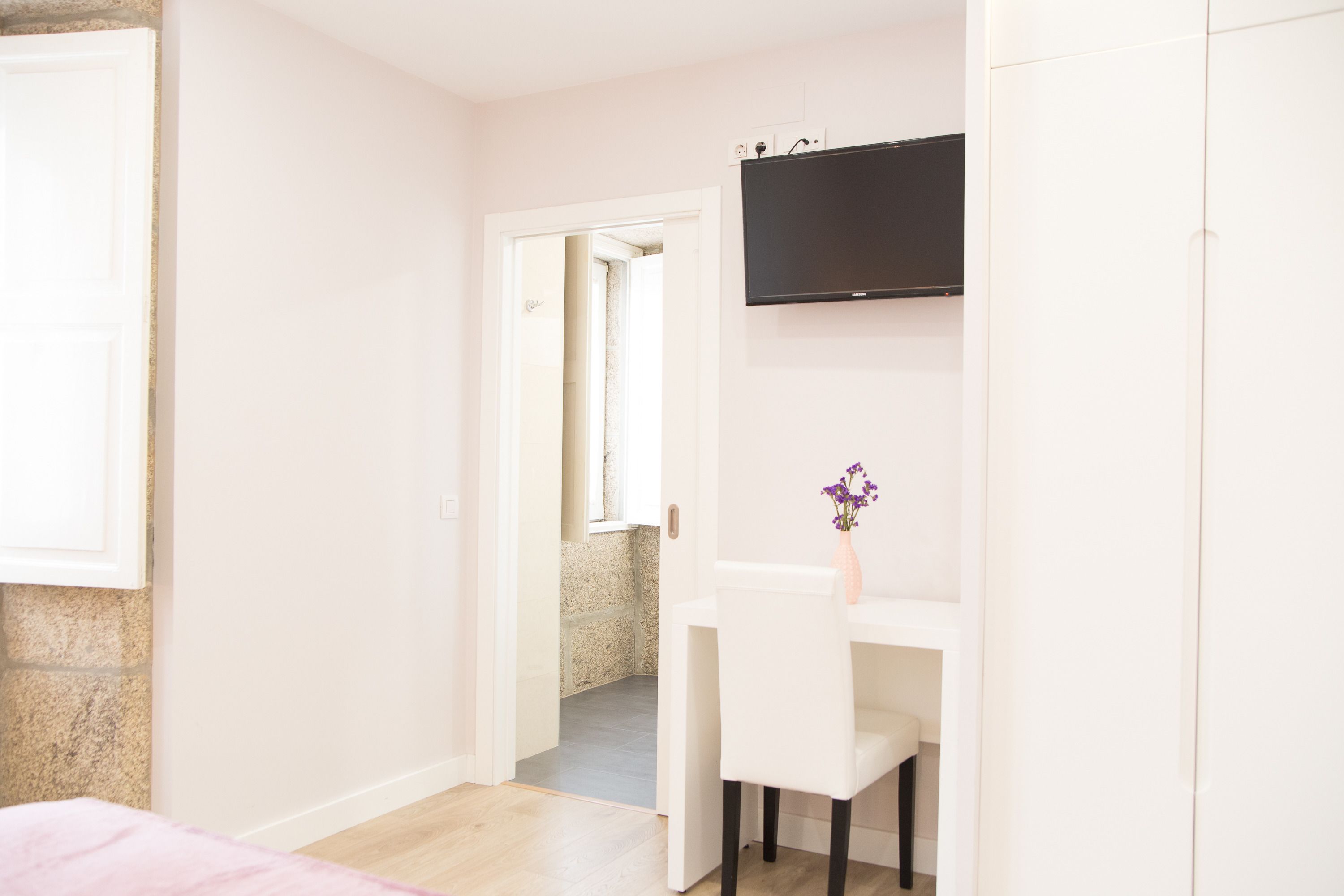 Une chambre d’hôtel avec un lit, un bureau et une chaise, un téléviseur fixé au mur et une salle de bain visible à travers une porte ouverte.