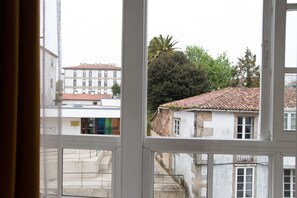 A view through a window of a building with a tiled roof, a tree, and another building in the background. - Linares Rooms Santiago (Santiago de Compostela)