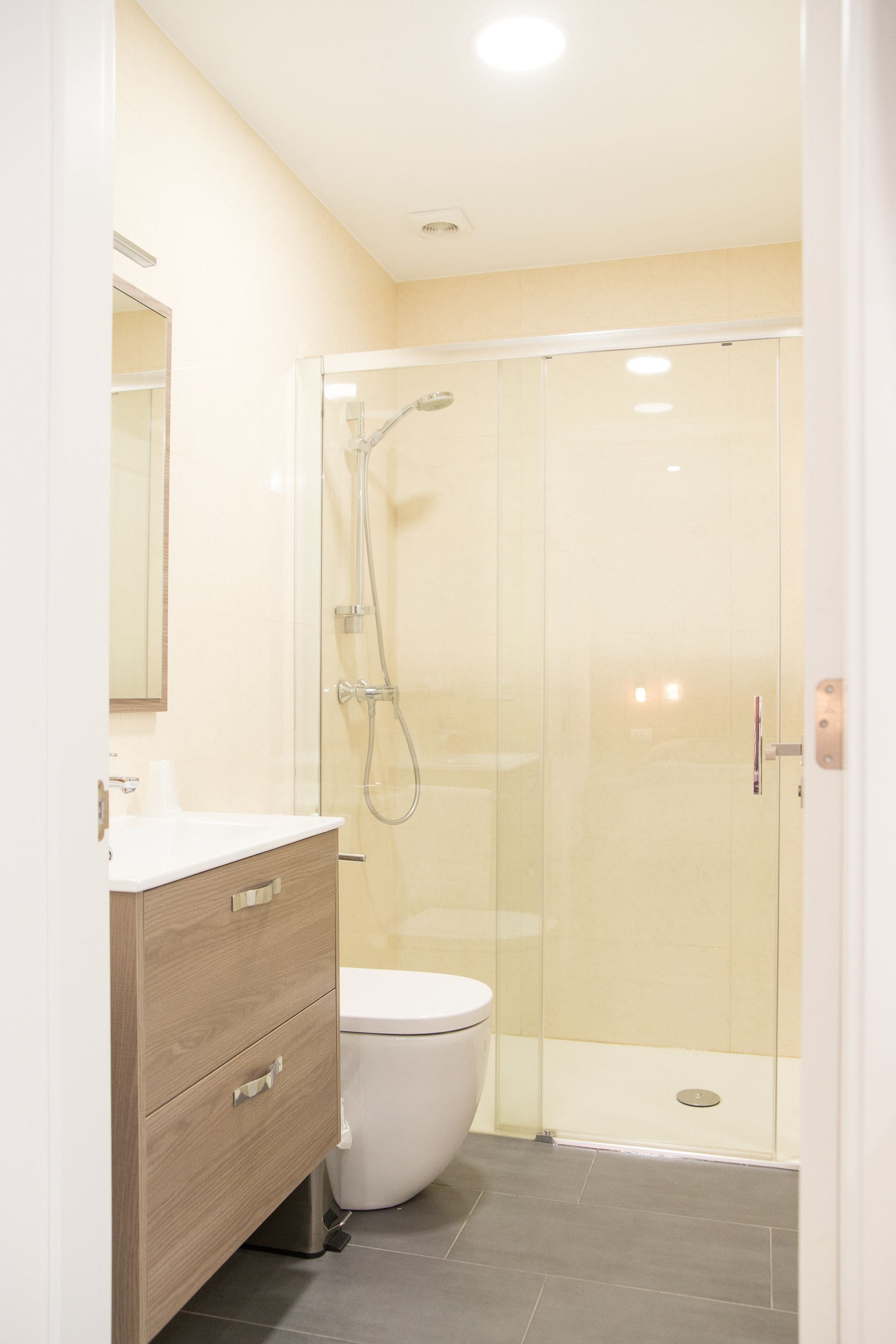 Une salle de bain moderne avec une douche à parois de verre, des toilettes blanches et un meuble-lavabo en bois doté de tiroirs.