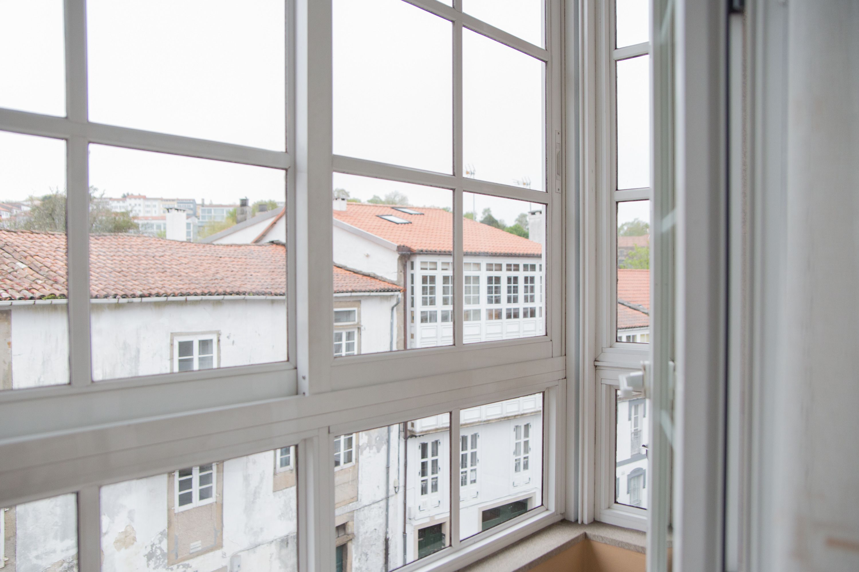 Vista a través de una ventana con entramado, mostrando edificios con tejados rojos y fachadas blancas.