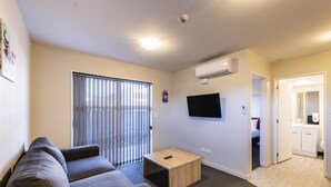 Un salón moderno con un sofá gris, una mesa de centro de madera y un televisor montado en la pared.