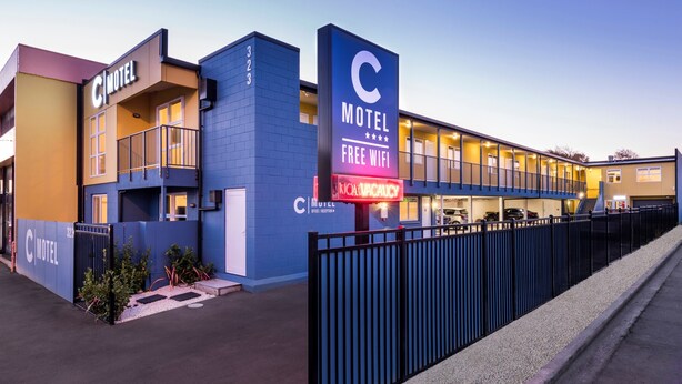 Un motel con un letrero grande en forma de 'C', un letrero que indica 'WiFi gratuito' y un letrero de 'No estacionar'.