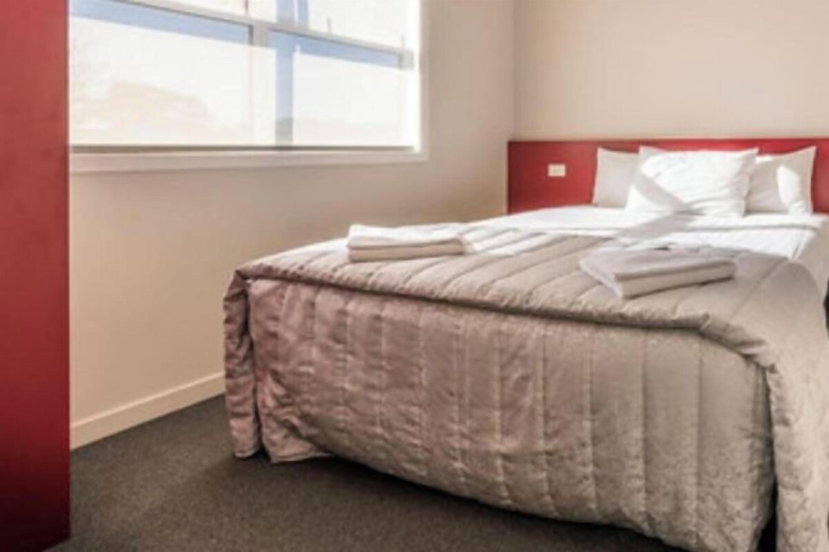 A hotel room with a bed, a window, and a red headboard.