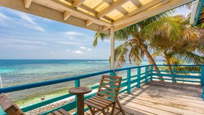 A wooden deck with a view of the ocean, a wooden chair, and a small round table. - Ranguana Caye Cabanas (Placencia)