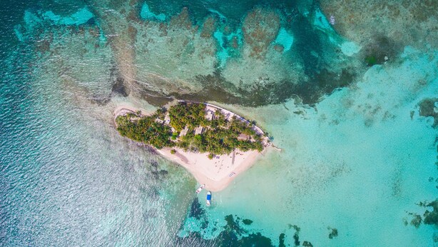 An aerial view of a small island with a beach, surrounded by clear turquoise waters. - Ranguana Caye Cabanas (Placencia)