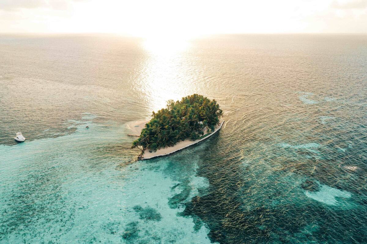 An aerial view of a small island with dense vegetation, surrounded by clear turquoise waters.