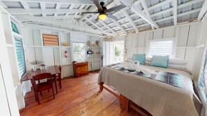 A room with a wooden floor, a bed with a patterned bedspread, a ceiling fan, and a window with blinds. - Ranguana Caye Cabanas (Placencia)