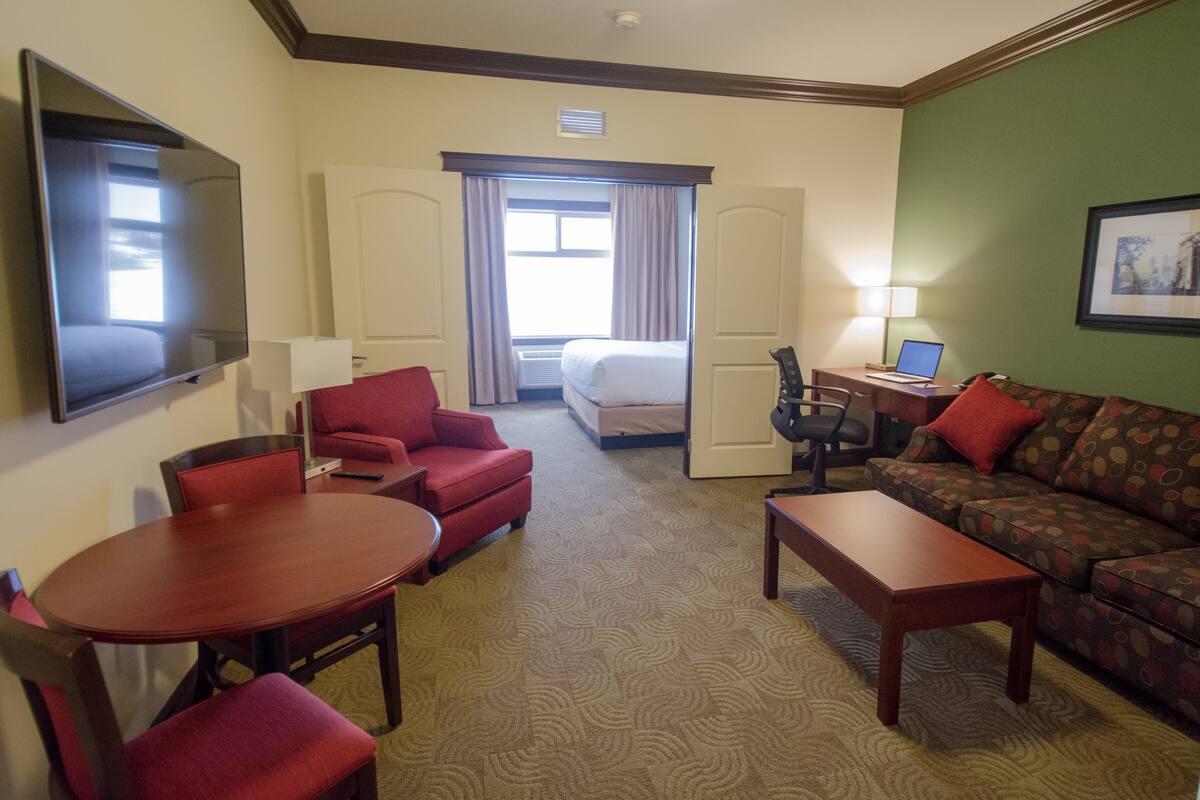 Een hotelkamer met een bed, een rode fauteuil, een bank, een eettafel en een televisie.