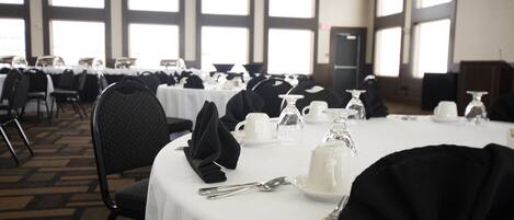 A banquet hall with round tables set for dining, featuring white tablecloths and black napkins.
