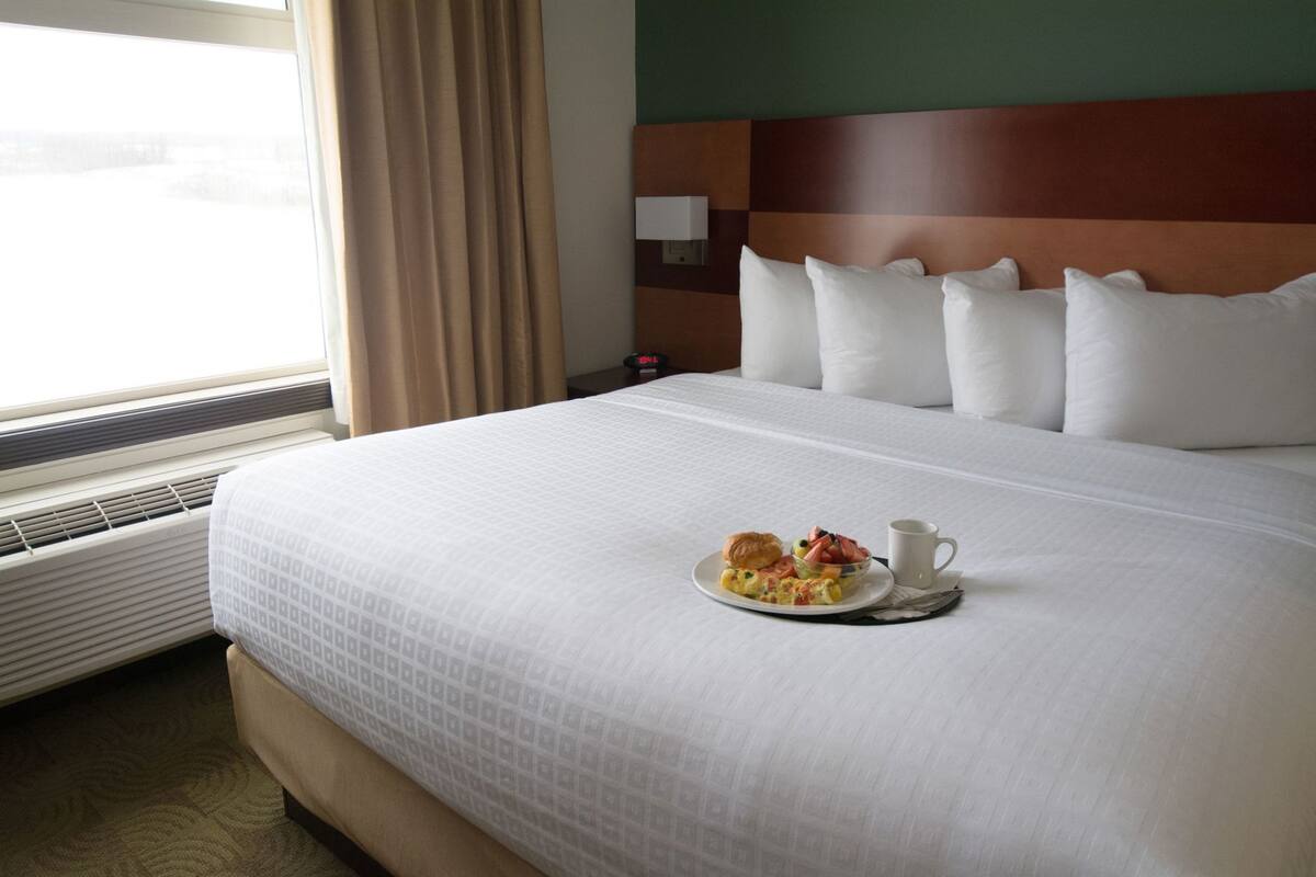 Een hotelkamer met een groot bed, een nachtkastje met een klok en een raam met gordijnen.
