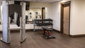 A gym with weightlifting equipment, a bench, and a rack of dumbbells.