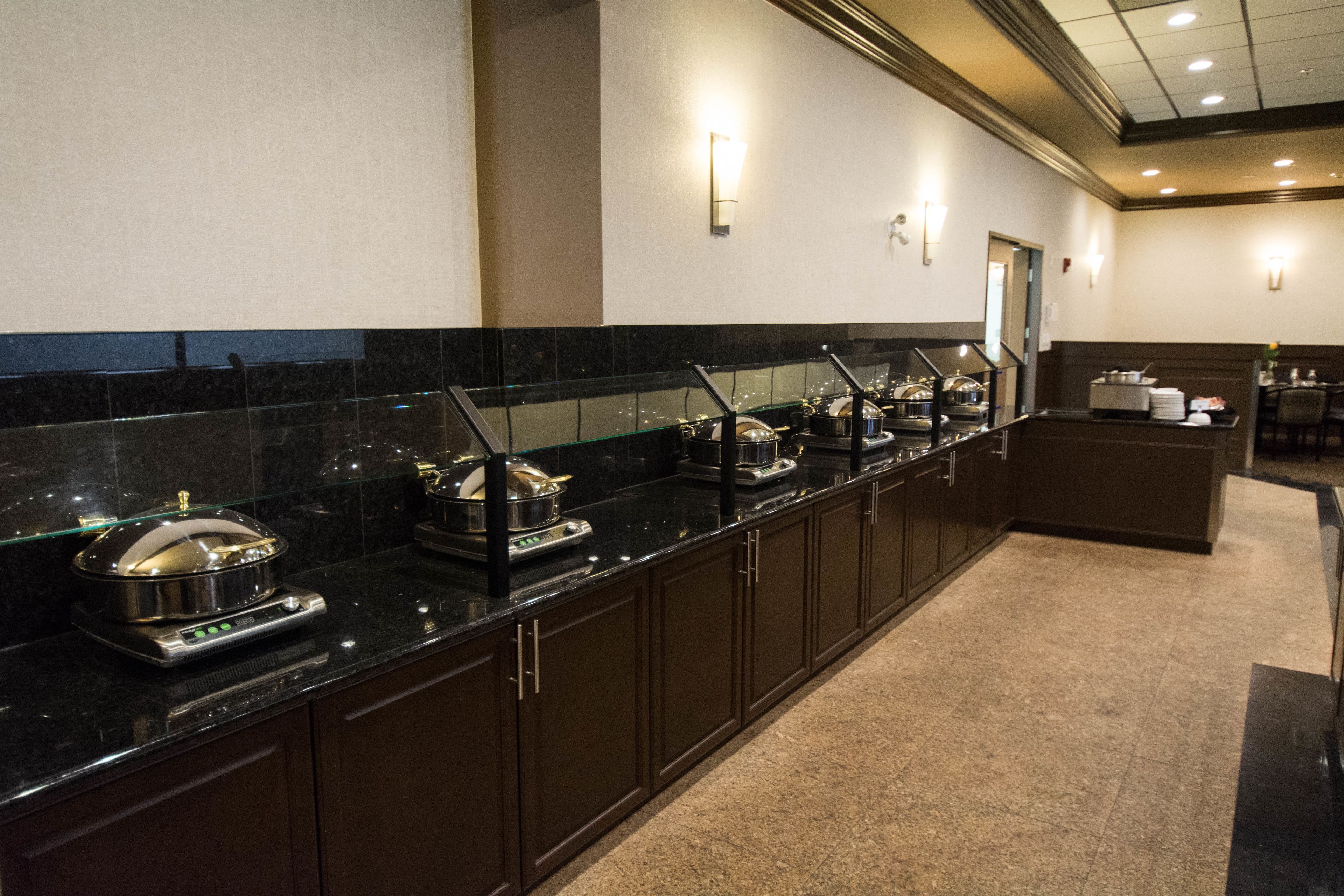A long buffet line with various food stations, a counter with a cash register, and a seating area in the background.
