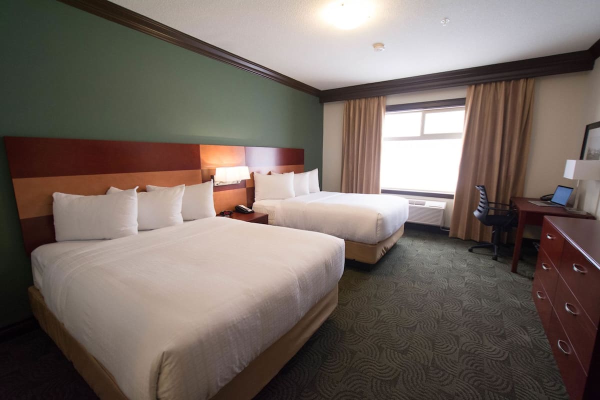 Een hotelkamer met twee bedden, een bureau, een stoel, een dressoir en een raam met gordijnen.