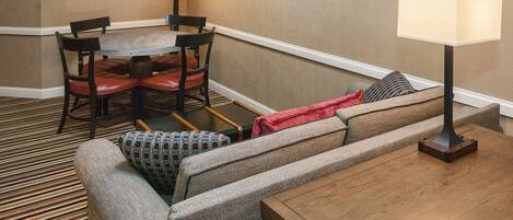 Habitación de hotel con zona de comedor, sofá, mesa de madera y dos lámparas de pared.