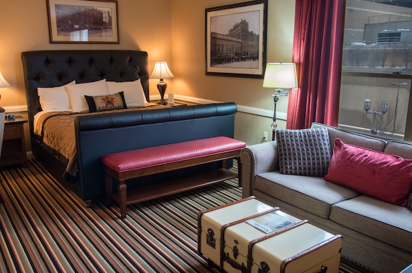 A hotel room with a large bed, a bench, a sofa, and a suitcase. - Fitger's Inn (Duluth)