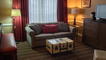 Une chambre d’hôtel avec un canapé, une petite table, un meuble et une valise.