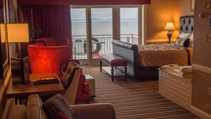 A hotel room with a bed, a sofa, a chair, a small table, and a view of the sea through large windows. - Fitger's Inn (Duluth)