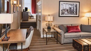 A hotel room with a dining area, a sofa, a red pillow, a framed picture, and a suitcase. - Fitger's Inn (Duluth)