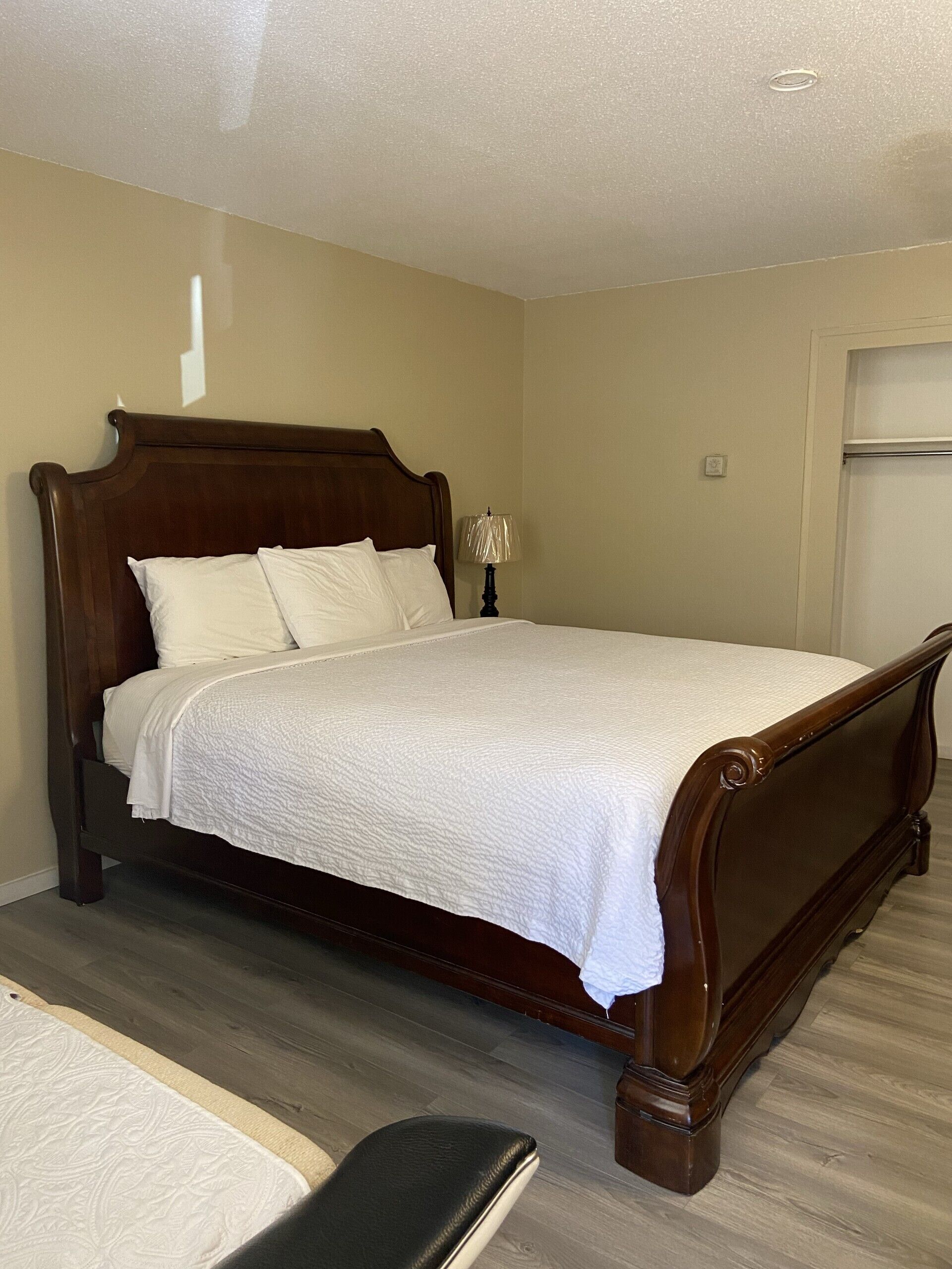 Una cama bien hecha, con tablero de madera y ropa de cama blanca, en una habitación con paredes color beige y suelo de madera.