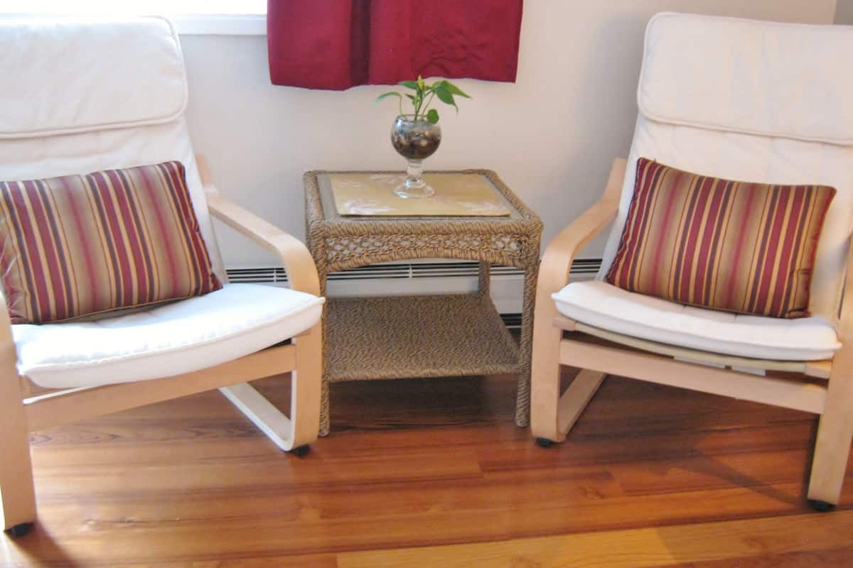 Two white chairs with striped cushions, a small woven table with a glass vase, and a red curtain in the background.