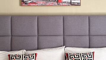 A room with a grey upholstered headboard, two patterned pillows, and a framed artwork depicting a red tree and the Eiffel Tower.