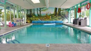 An indoor swimming pool with a mural of a forest scene, lounge chairs, and a lifebuoy. - Slumber Lodge Motel (Hope)