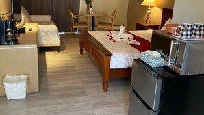 A hotel room with a bed, a desk, a refrigerator, a coffee maker, a table with a vase of flowers, and a chair. - Slumber Lodge Motel (Hope)