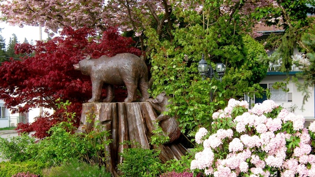 A garden with a bear statue on a wooden stump, surrounded by various shrubs and flowers. - Slumber Lodge Motel (Hope)