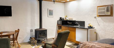A cozy room with a wooden ceiling, a fireplace, a dining table, a kitchen area, and a bed.