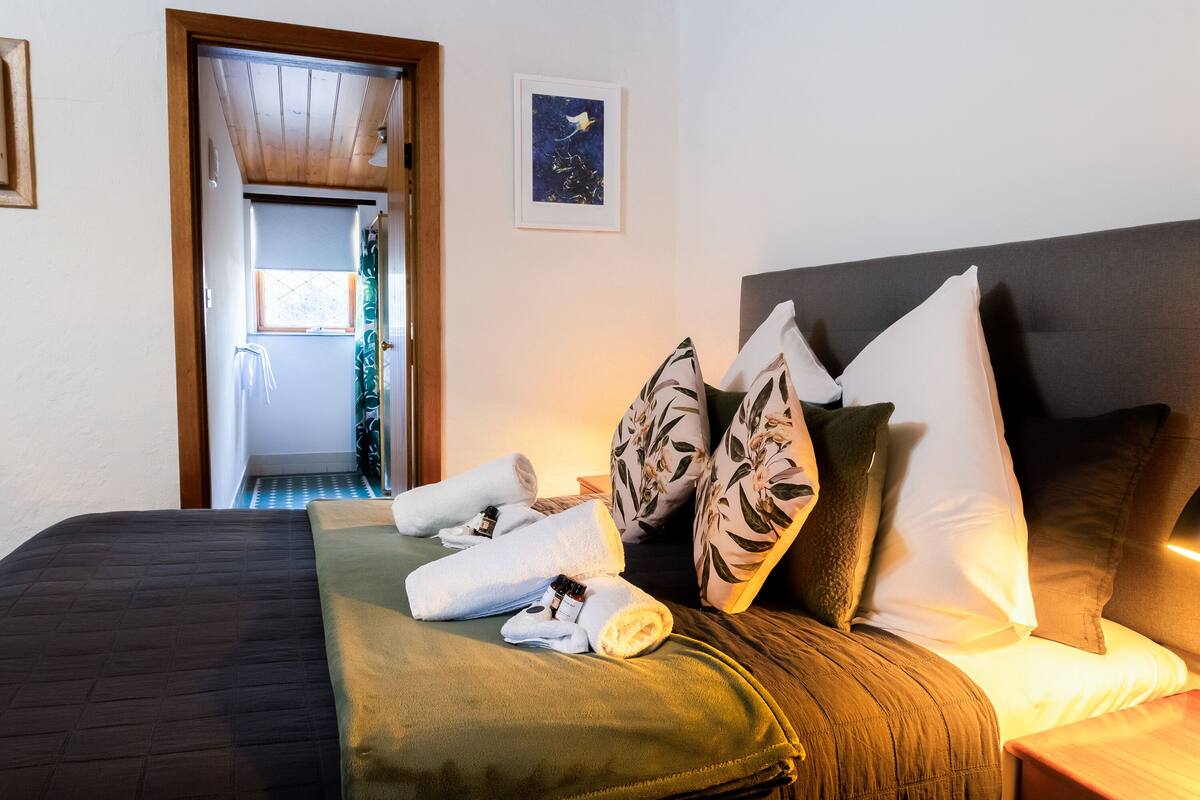 A neatly made bed with towels and pillows, a wooden headboard, and a framed picture on the wall.