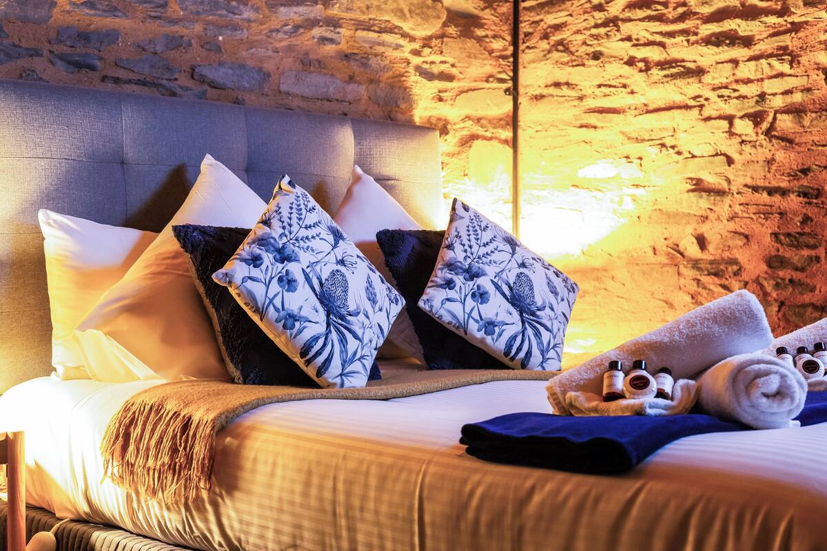 A bed with a headboard, multiple pillows, a blanket, and toiletries.