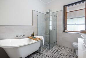 A bathroom with a freestanding bathtub, a glass-enclosed shower, a toilet, and a window with a view. - Reillys Wines Heritage Cottages (Mintaro)