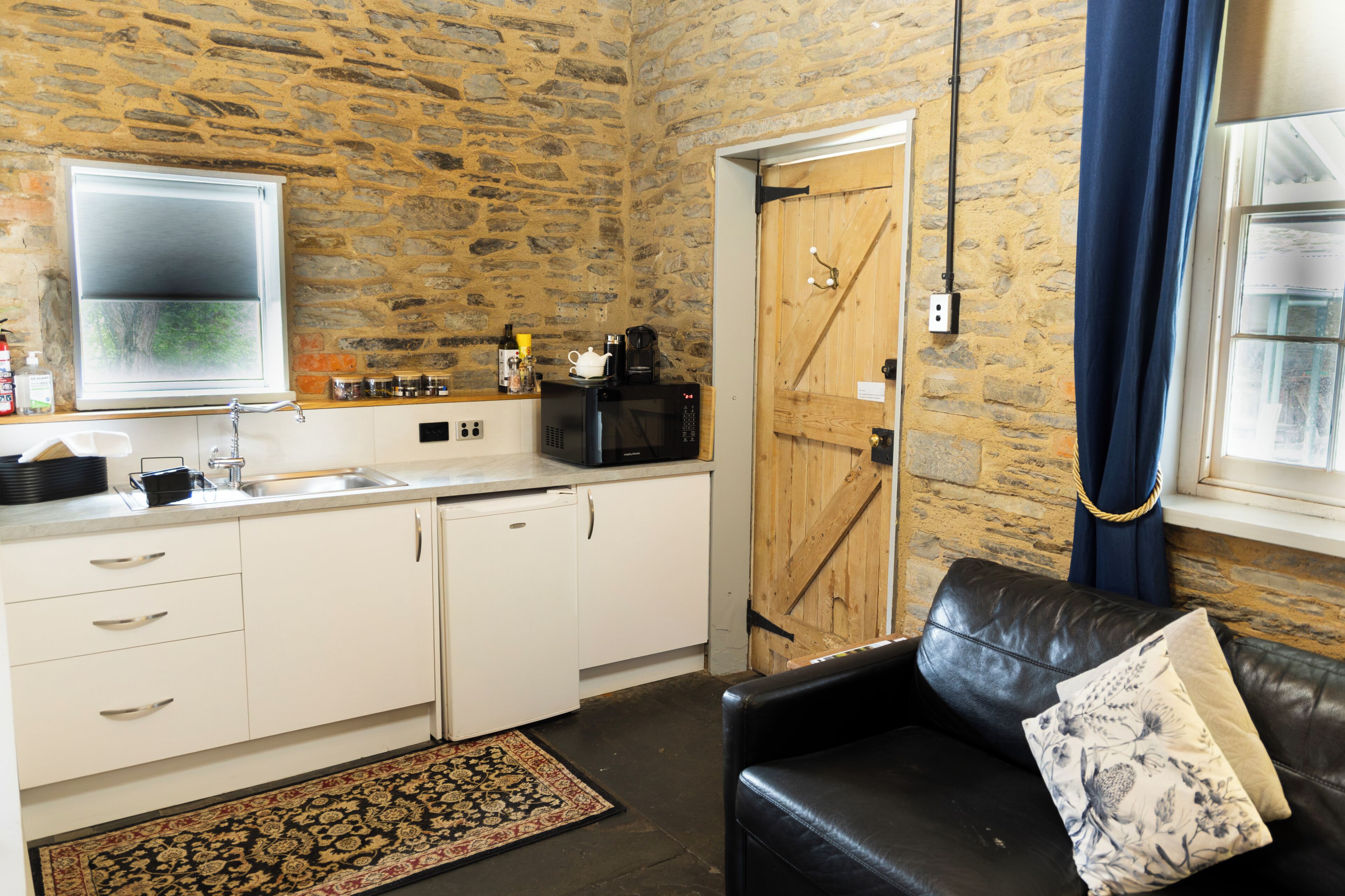A stone-walled kitchen with a sink, cabinets, and a coffee machine.