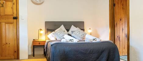 Een slaapkamer met een bed, nachtkastje, lamp en een ventilator aan de muur.