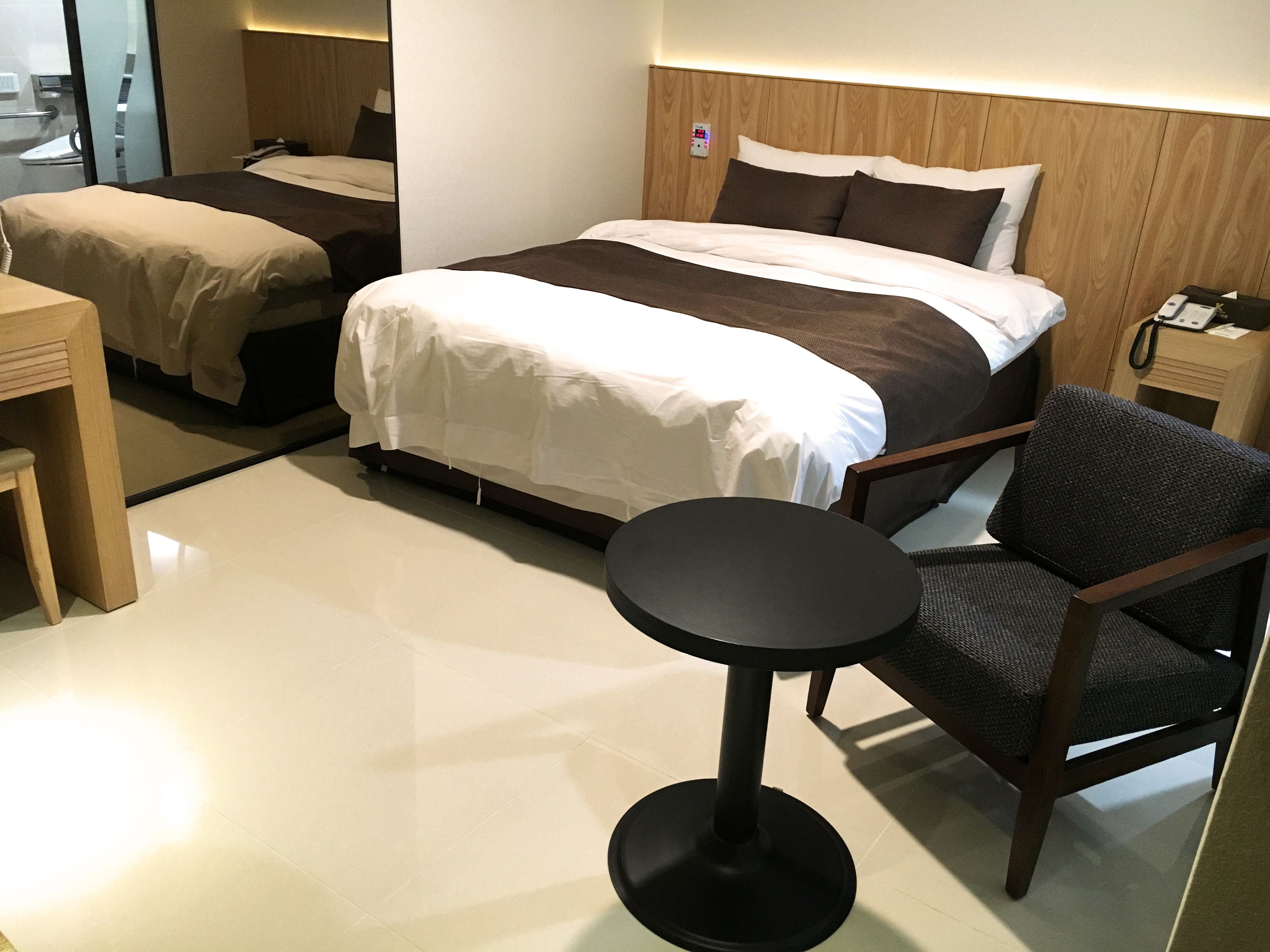 Una habitación de hotel con una cama grande, una cama más pequeña, un escritorio, una silla y una mesita de noche.