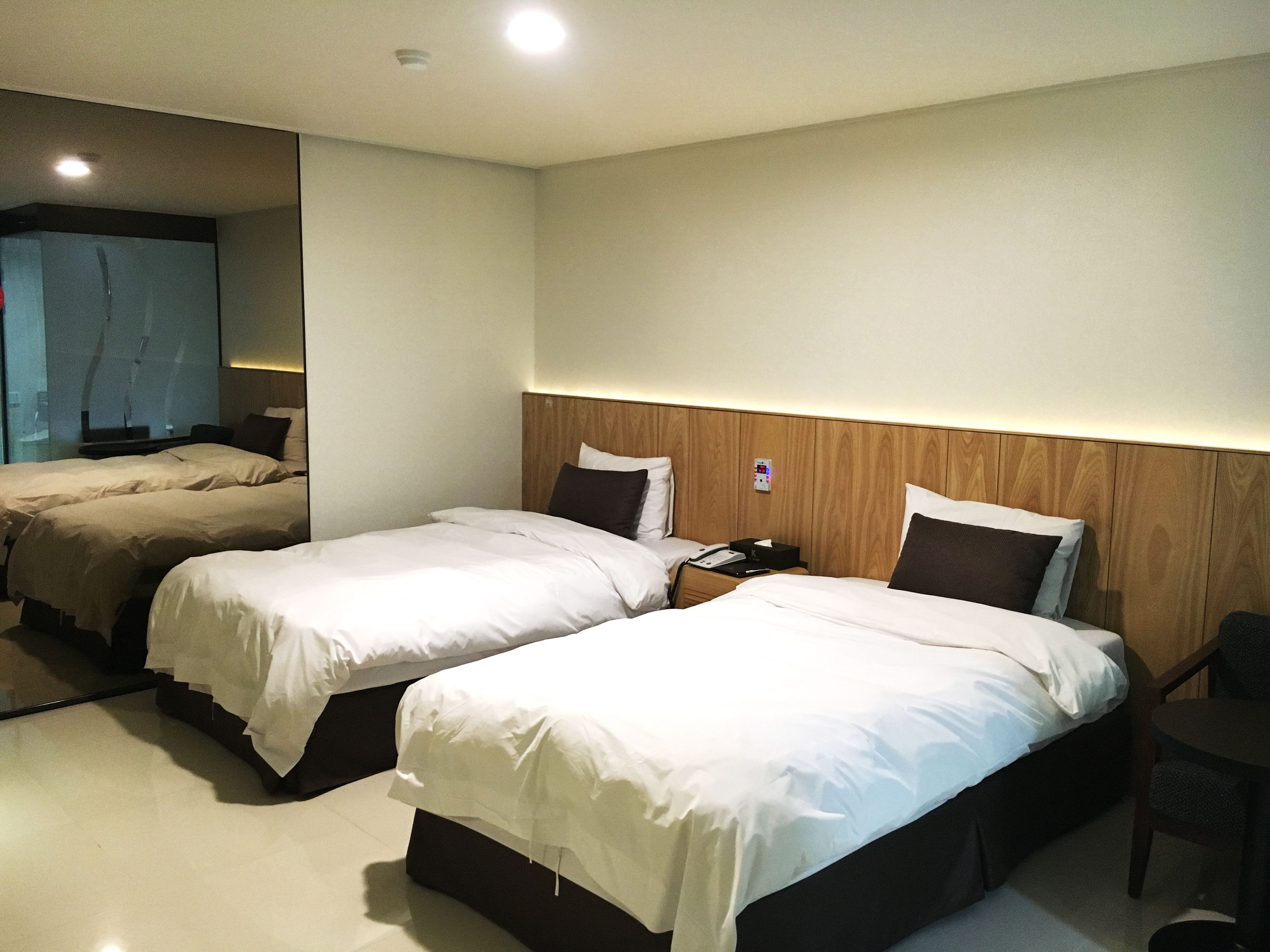 A hotel room with two beds, a bedside table with a phone and a lamp, and a small chair.
