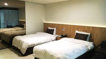 A hotel room with two beds, a bedside table with a phone and a lamp, and a small chair.