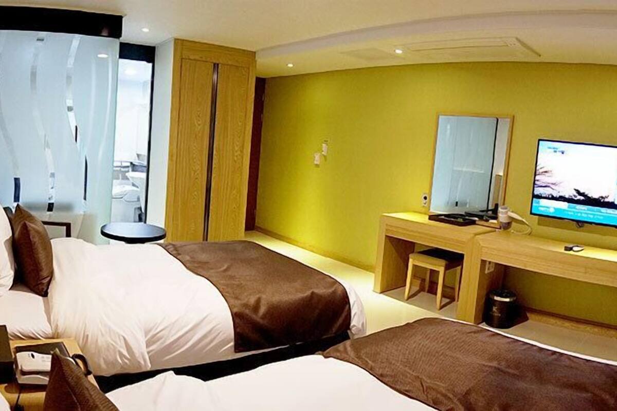 A hotel room with two beds, a desk with a computer, a TV, and a window with curtains.