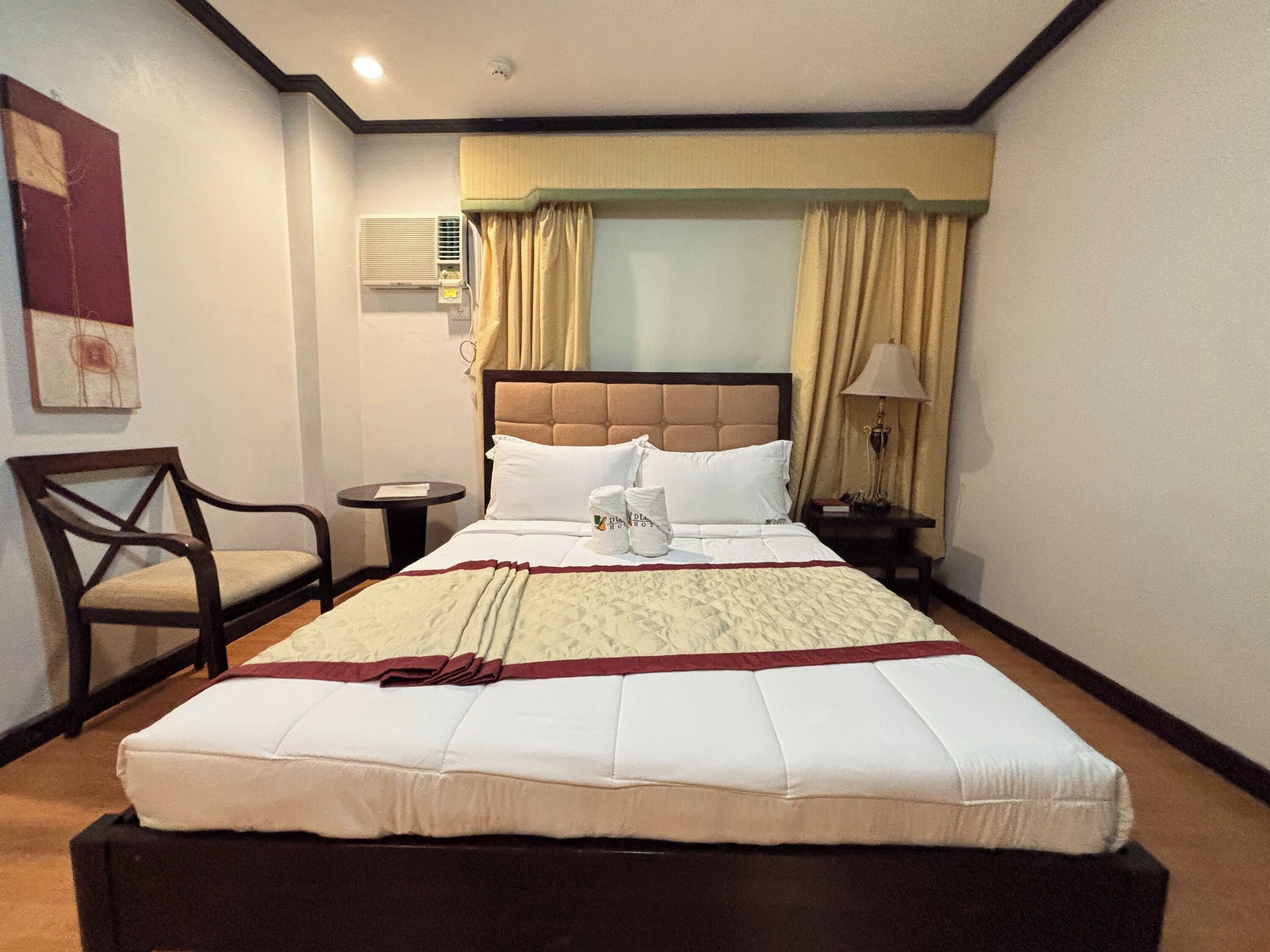 A hotel room with a large bed, a chair, a bedside table, and a lamp.