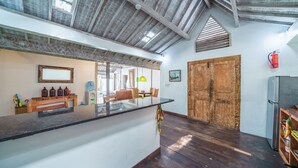 A spacious kitchen with a large island, wooden ceiling beams, and a rustic wooden door. - Villa West (Seminyak)
