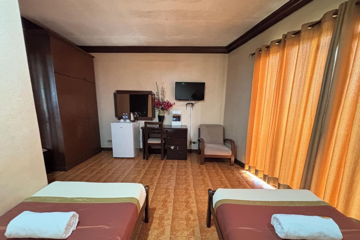 A hotel room with two beds, a desk with a chair, a television, and a refrigerator.