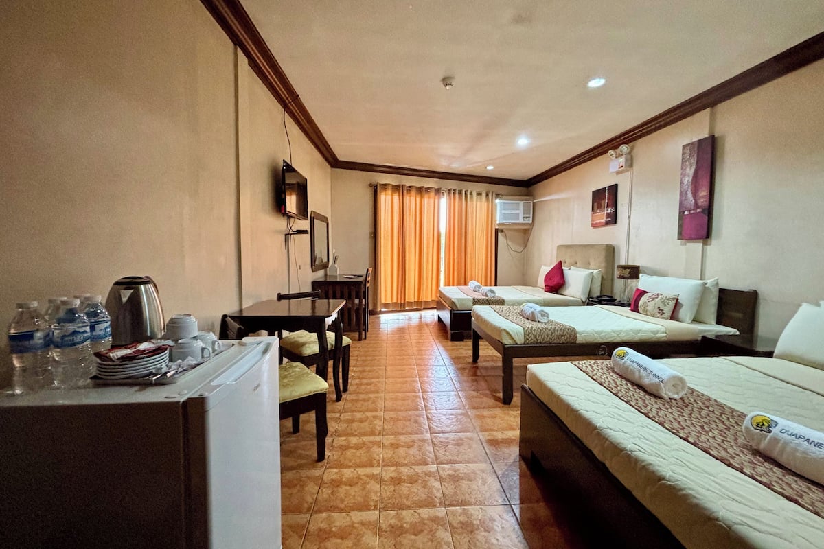 A hotel room with two beds, a dining table, a refrigerator, and a TV.