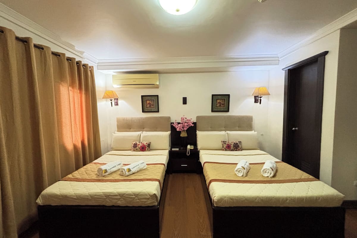 A hotel room with two beds, a nightstand with a lamp, a wall-mounted air conditioner, and a door.