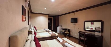 A hotel room with two beds, a desk, a television, and a small kitchenette.