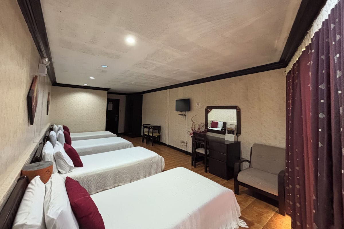 A hotel room with three beds, a desk, a chair, and a television.