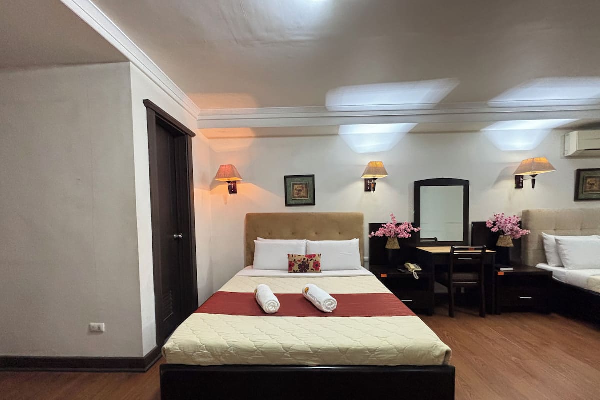 A hotel room with a bed, bedside lamps, a desk, a chair, a sofa, and a mirror.