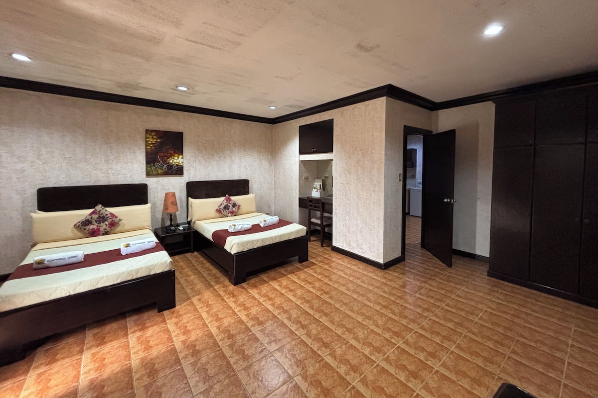 A hotel room with two beds, a desk, a chair, a wardrobe, and a bathroom visible through an open door.