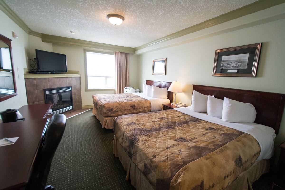 A hotel room with two beds, a television, a fireplace, a desk, and a framed picture on the wall.