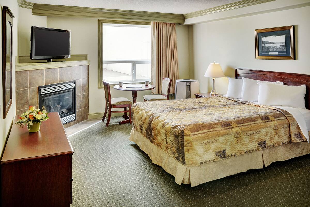 A hotel room with a bed, a television, a fireplace, a desk, and a window with curtains.