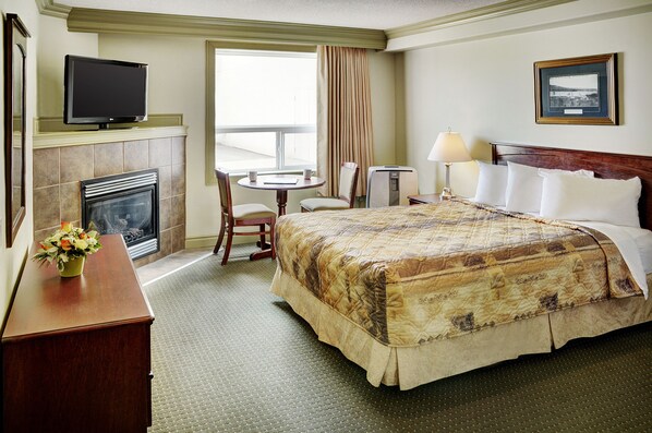 A hotel room with a bed, a television, a fireplace, a desk, and a window with curtains. - Nova Inn Peace River (Peace River)
